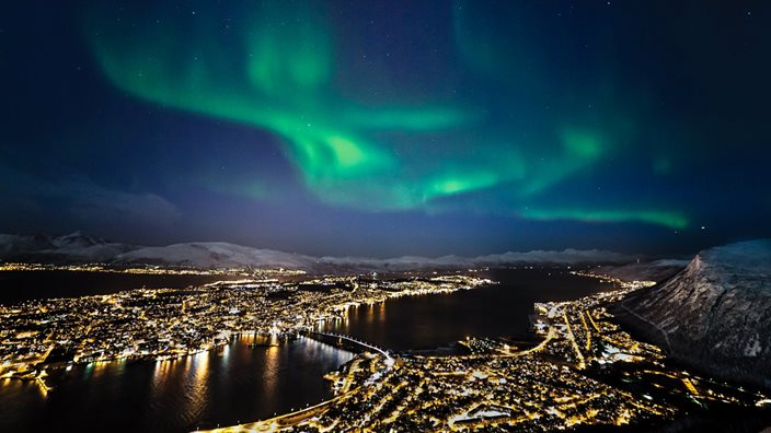 Northern Lights dancing over Tromsø, Norway, above snow-covered mountains and a starry sky